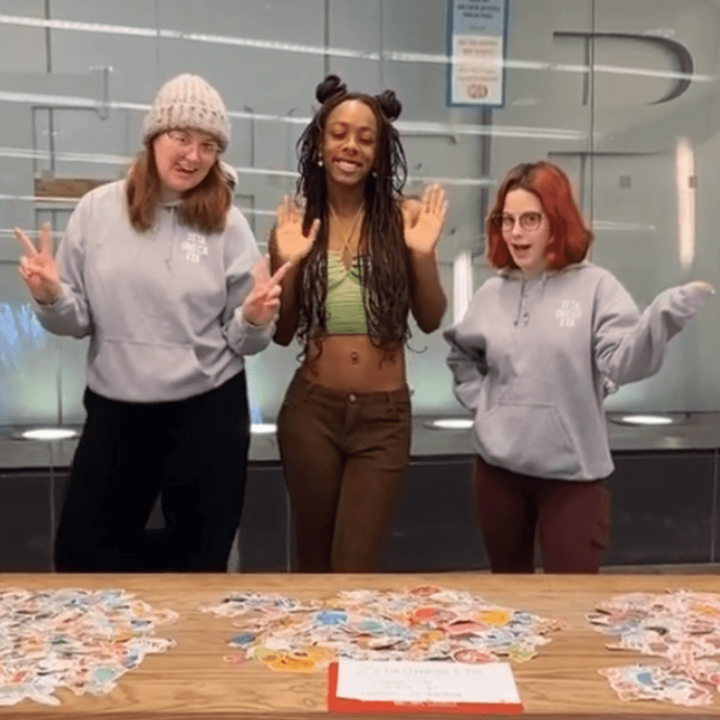 image of three college women posing in front of a table spread with colorful stickers