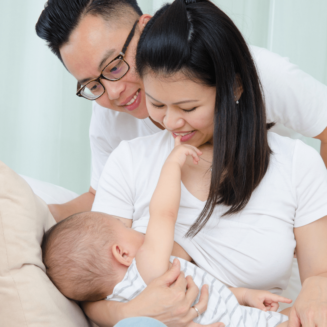 man and woman in white shirts smiling down at breastfeeding infant